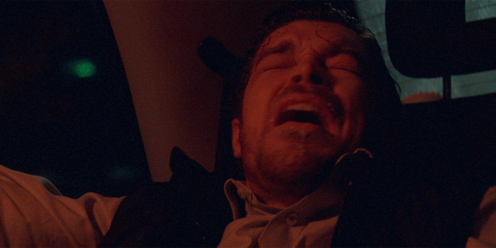 A man looking distressed in red light in a taxi