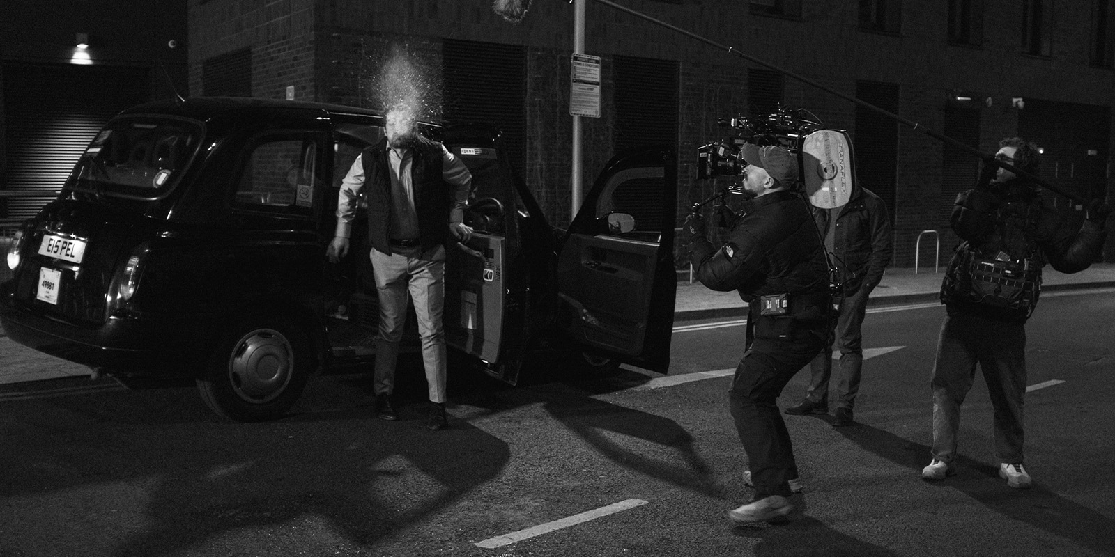 Film crew filming a man spitting by a taxi