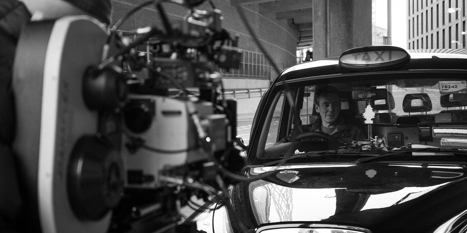 A film camera filming a man in a taxi