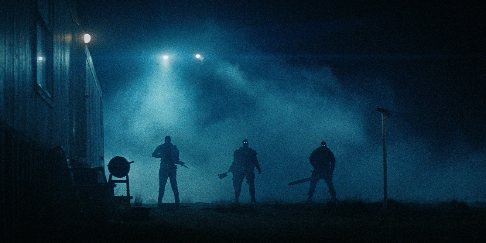 Three people holding weapons stand in front of a building at night, backlit by headlamps shining through fog, creating a dramatic and tense atmosphere.